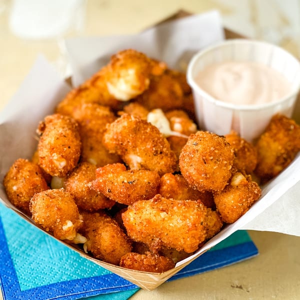 Golden-brown fried cheese curds in a paper tray with a side of dipping sauce.