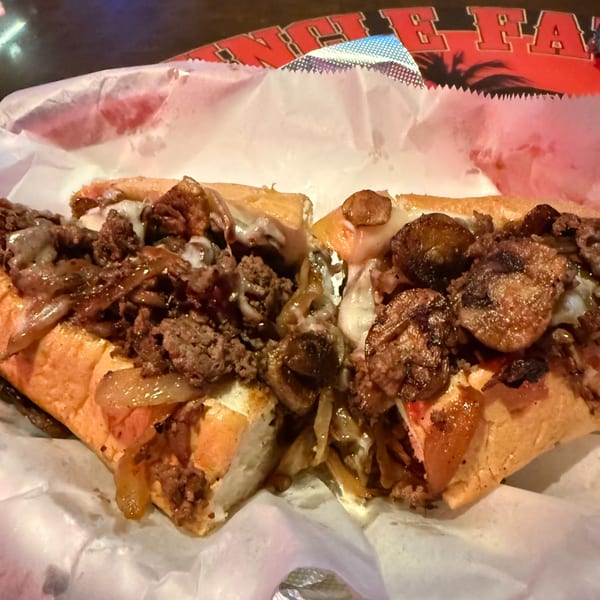A close-up of a hearty cheesesteak sandwich from Uncle Fats Tavern, overflowing with meat, onions, and mushrooms.